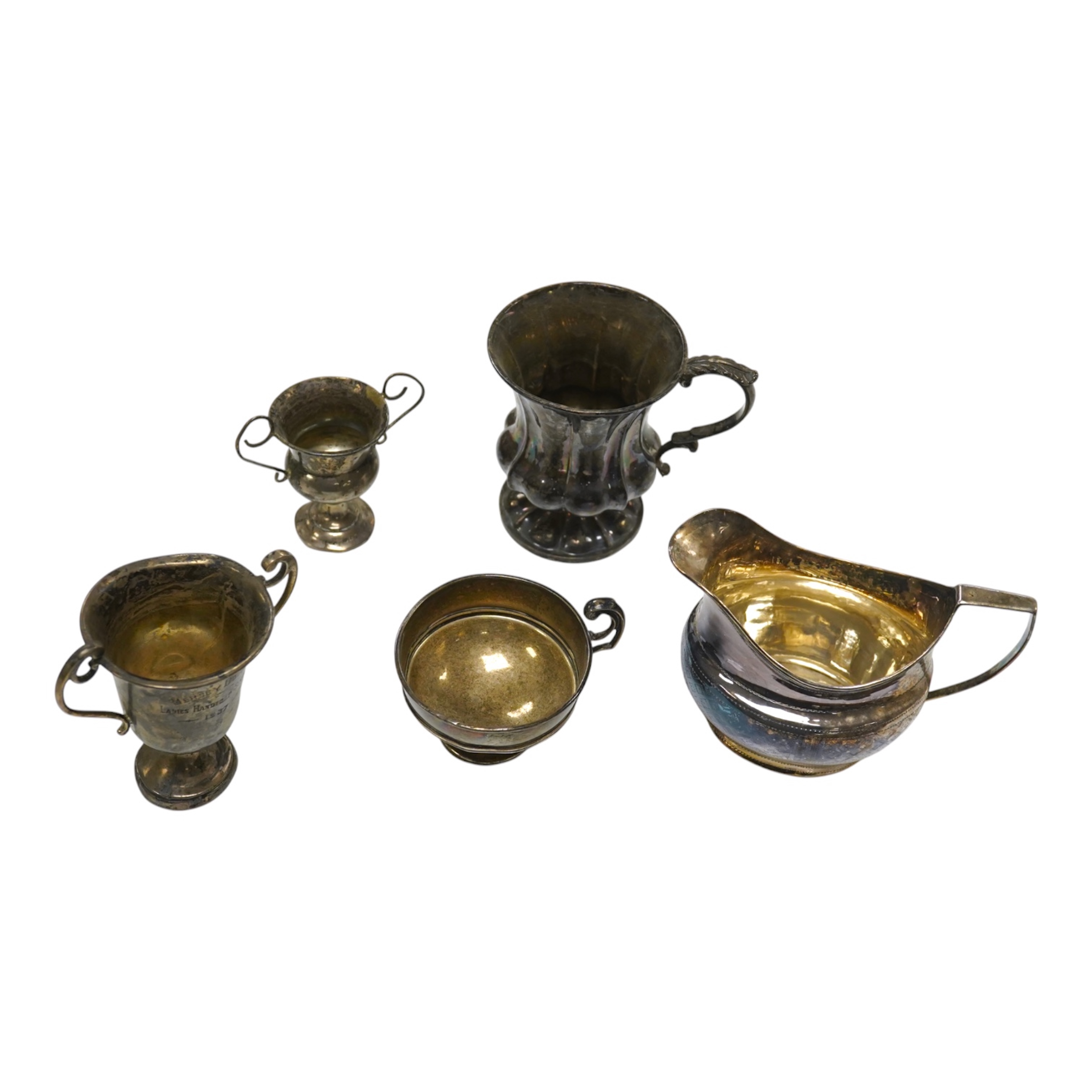 A William IV silver christening mug, London 1834, 10cm, a George III silver cream jug, London, 1799 and three small silver trophy cups. Condition - poor to fair